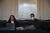 Angela Furmaniak (lange dunkelbraune Haare) und Fabian (kurze braune Haare), sitzen am Verhandlungstisch. Angela Furmaniak hat einen Laptop vor sich aufgeklappt.