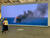 Zwei Personen schauen auf eine etwa drei Meter hohe Leinwand auf der ein Video von einem brennenden Fischkutter auf dem Mittelmeer läuft. Eine Person steht an Bord des Boots. Adel Abdessemed: Jam Proximus Ardet, la derniére vidéo. 2021. Galleria Continua.