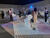 Personen in einem Raum mit ein paar Quadern und Luftballons werden von allen Seiten mit Streifen von Licht angebeamert. Carlos Cruz-Diez: Environnement Chronointerferent, 1974/2018. Galleria Continua. San Gimignano. Art Basel Unlimited.