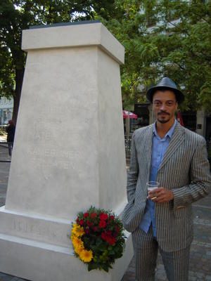 Künstler Philip Metz neben dem Denkmal Le Héros Invisible. Auf dem Denkmal steht: &quot;Zu Ehren der für das deutsche Vaterland gefallenen kameruner Soldaten – 1914-1918&quot;