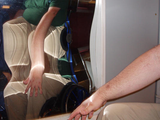 Ein Foto von einem Zerrspiegel, der ein verzerrtes Bild vom Arm einer Person im Rollstuhl zeigt.
