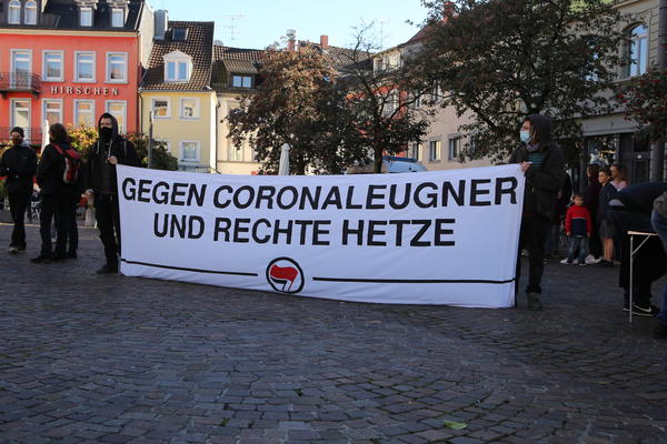 Ein weißes Transparent mit schwarzer Schrift: "Gegen Coronaleugner und rechte Hetze", sowie ein Antifasymbol.
