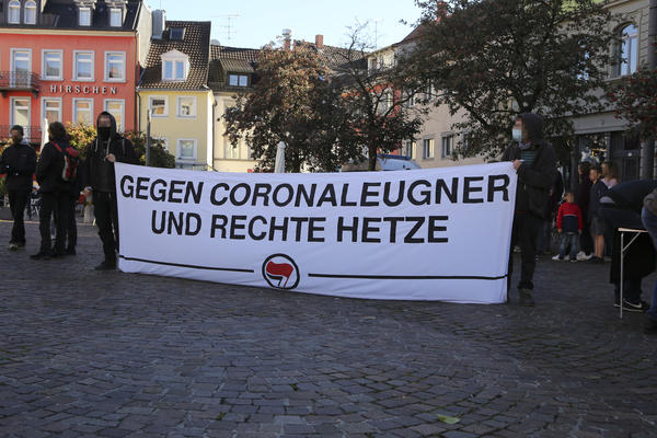 Weißes Transparent, auf dem in schwarzer Schrift steht: &quot;Gegen Coronaleugner und rechte Hetze&quot;. Außerdem Antifa-Symbol.