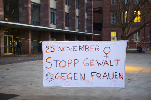 Ein weißes Transparent auf dem Platz der Alten Synagoge, auf dem steht: &quot;25. November - Stopp Gewalt an Frauen&quot;. Ergänzt durch das Frauensymbol in der rechtsobigen Ecke und Handabrücke auf der Unterseite.