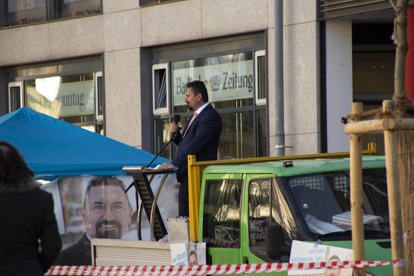 Mandic hetzt auf dem Lörracher Marktplatz. Im Hintergrund sieht man die Logos von der Badischen Zeigung und Dem Sonntag, in der Schaufensterscheibe.