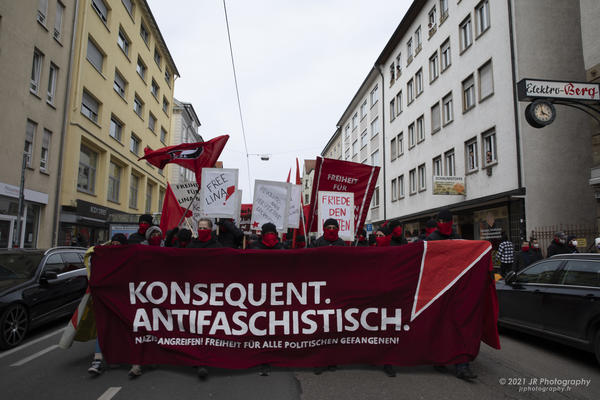 Demonstrationsfront mit rotem Transparent auf dem in weißen Großbuchstaben steht: Konsequent antifaschistisch.