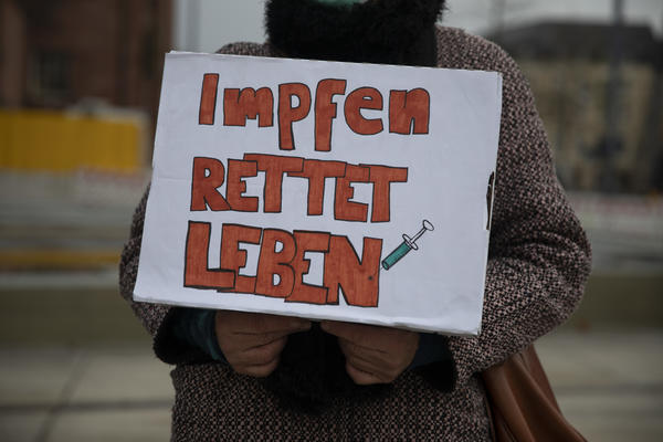 Ein auf Brusthöhe gehaltenes Schild, auf dem in roten Großbuchstaben steht: Impfen rettet Leben.