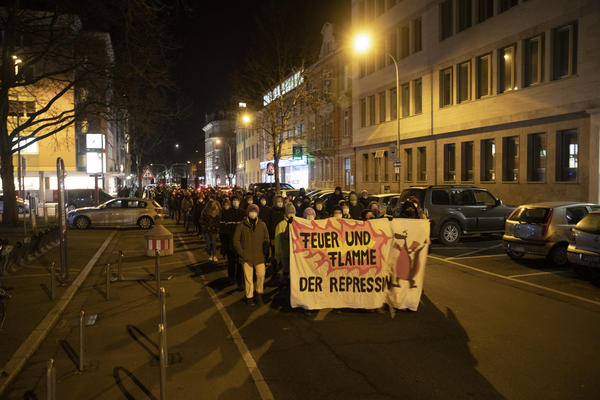 Ein Demonstrationszug bei Dunkelheit in der Rempartstraße. Auf dem Fronttransparent ist ein Drache abgebildet und es steht &quot;Feuer und Flamme der Repression&quot; darauf.