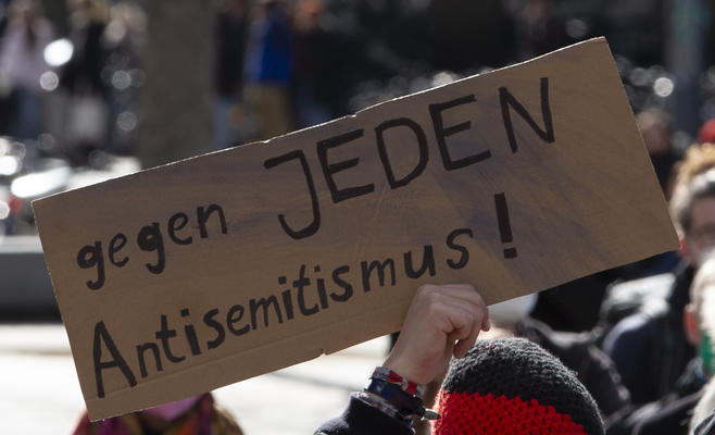 Bildausschnitt eines Schildes, das mit einer Hand in die Luft gehalten wird. Darauf steht: &quot;Gegen jeden Antisemitismus!&quot;