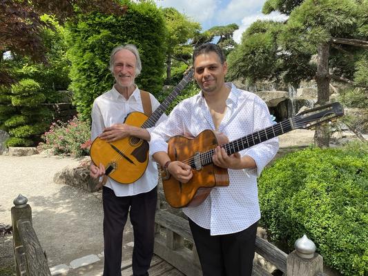 Angelo Brand und Helmut Lindler in weißen Hemden mit Gitarren vor einem Garten