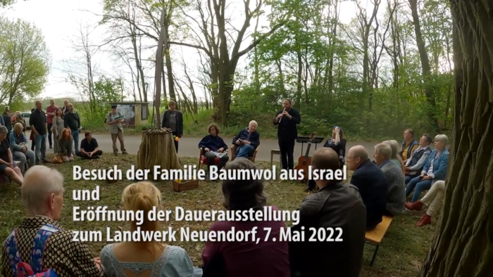 Besuch der Familie Baumwol aus Israel - eine Gruppe Menschen sitzt im Wald um die mit Blumen geschmückte Statue der ermordeten Jutta Baumwol