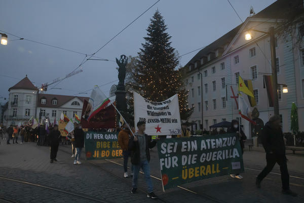Ein Demonstrationszug startet vom Europaplatz Richtung Bertoldsbrunnen. Im Hintergrund das &quot;Siegesdenkmal&quot; und ein Weihnachtsbaum zu sehen. Auf dem Fronttransparent steht: Sei ein Atemzug für die Guerilla überall&quot;. Viele YPG- &amp; andere kurdische Fahnen.