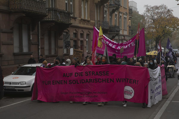 Demonstrationszug im Stühlinger. Pinkes Fronttransparent: Auf die Straße - Für einen solidarischen Winter. Unten steht: Gegen Preissteigerungen, Heizkosten und diese Krisenpolitik.