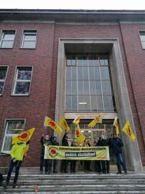 Menschen stehen mit einem Banner (&quot;Schrottreaktor Neckarwestheim - endlich abschalten&quot;) vor dem Gebäude des Verwaltungsgerichtshofs Baden-Württemberg