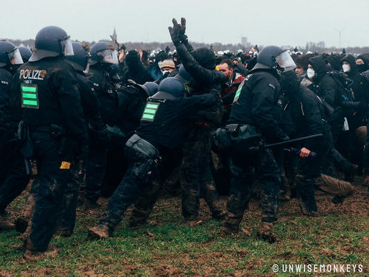 Behelmte Polizei schubst eine demonstrierende Person, die die Hände zu Peace Zeichen erhoben hat