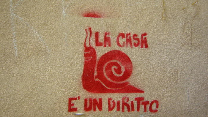 Graffiti auf einer Wand in Rot, eine Schnecke ist dargestellt, mit dem Schriftzug &quot;La Case e un diritto&quot;