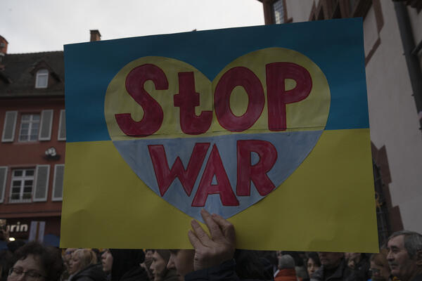 Ein Schild mit den Farben der Ukraine wird ins Bild gehalten. Ein Herz ist abgebildet, mit invertierten Faben (gelb-blau) und darauf die Worte: Stop War
