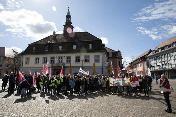 Auf dem Marktplatz in Emmendingen stehen Streikende versammelt, ganz rechts Person mit Megafon zur Menge gerichtet. Es ist leicht bewölkt, aber die Sonne scheint.