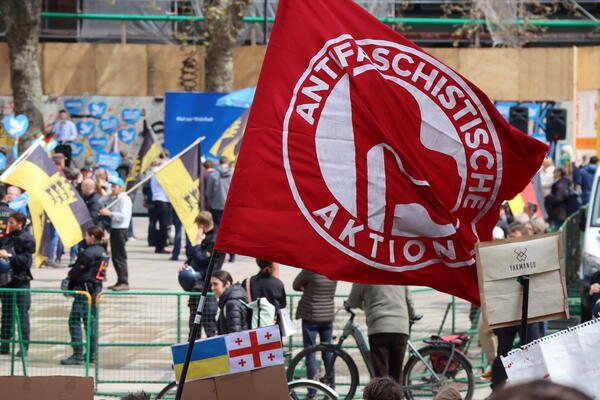 Eine rote Flagge: Antifaschistische Aktion. Dahinter auf dem Platz der Alten Synagoge sind Baden-Württembergflaggen und die Farben der AfD auszumachen