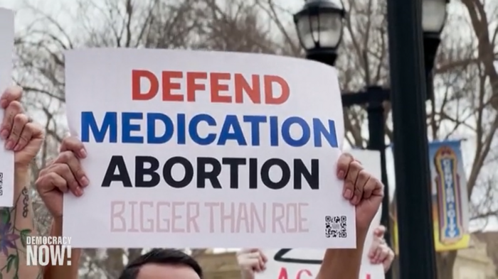 Ein Plakat wird von einer Person hochgehalten, die nicht im Bild ist: Defend Medication Abortion. Bigger than Roe