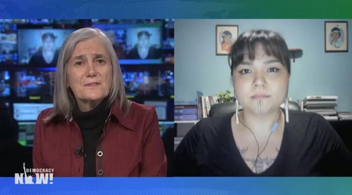 Split-Screen: Links Amy Goodman im Studio von DemocracyNow! mit Bildschirmen im Hintergrund; rechts SIDIÑIQ MAUPIN mit Stöplen im Ohr und Indigenen BIldern im Hintergund an der Wand