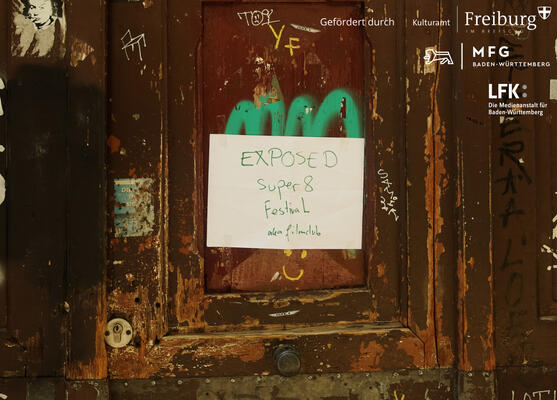 Eine verranzte Holztür zerkratzt mit Graffitis und einem Zettel: EXPOSED Super 8 Filmfestival aka filmclub