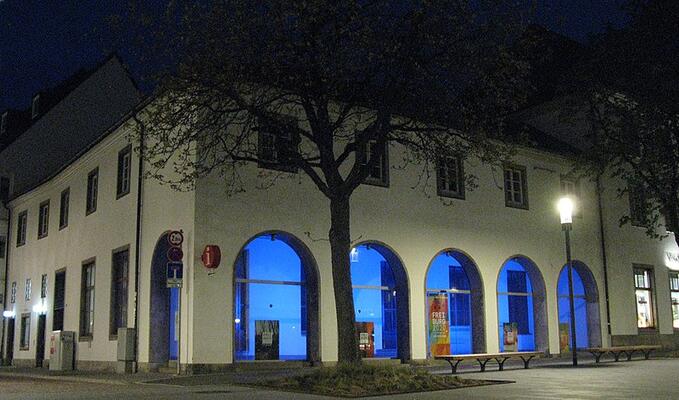 Das frühere Verkehrsamt auf dem Freiburger Rotteckring bei Nacht; die Bögen sind in blaues Licht getaucht; darin steht das Logo von Freiburg 2020
