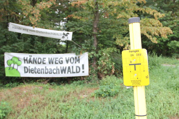 Im Vordergrund Schild der Gashochdruckleitung auf Grünstreifen südlich Munzingerstr. Im Hintergund Transpis gegen neue Trassenführung