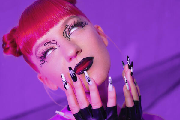 Nahaufnahme von Mariybus Gesicht, inklusive Nail-Art, Make-Up und roter Frisur 