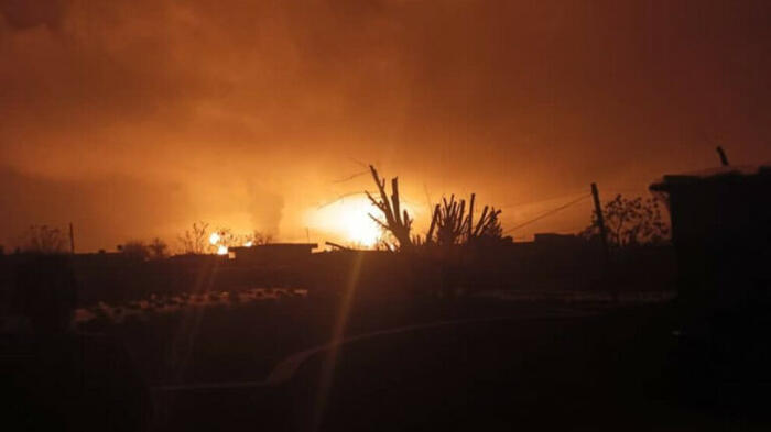 Explosion über einer ländlichen Region - die Flammen erhellen den Himmel, vereinzelt heben sich nur Gewächse und Häuser als Silhouetten ab