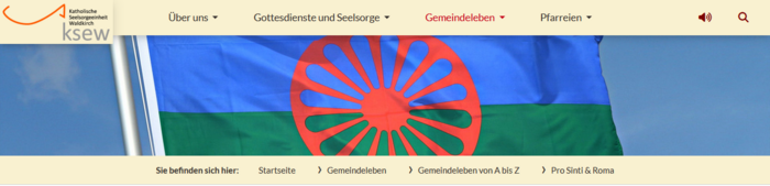 Die Roma-Flagge - das rote Rad vor blauem und grünem Hintergrund - auf der Website der Katholischen Seelsorge Waldkirch