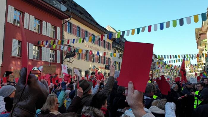 Das Bild zeigt eine große Menschenmenge im Zentrum der Stadt Waldshut, die rote Karten nach oben halten.
