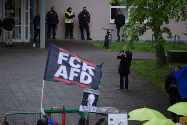 Im Vordergrund sind eine &quot;FCK AFD&quot;-Fahne zu sehen und ein Schild mit &quot;Gauländer raus!&quot;, von der APPD und paar Schirme von den Omas gegen Rechts. Dahinter ist Robert Hagerman zu sehen, wie er den antifaschistischen Protest gegen die AfD abfilmt.