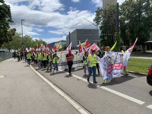 Demonstrationszug der Streikenden Uniklinikbelegschaft. Gelbe Warnwesten und rot-weiße Verdifahnen dominieren das Bild.