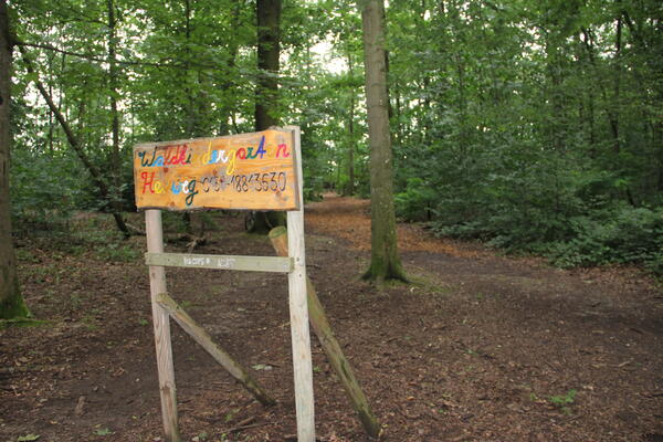 Zugangsschild zum Waldkindergarten Heuweggruppe im Langenmatten Wäldchen mit Bauwagen im Hintergrund