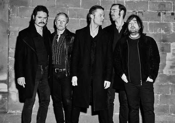 Die Band Mando Diao: Fünf mittelalte Männer stehen vor einer Wand und schauen zum Teil zur Seite zum Teil in die Kamera. Das Bild ist in Schwarz-WEiß