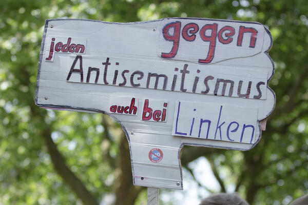 Ein weißes Schild, auf dem steht: &quot;gegen jeden Antisemitismus auch bei Linken&quot;. Ein kleiner, runder Aufkleber, auf dem AfD durchgestrichen ist, ist auch zu sehen.