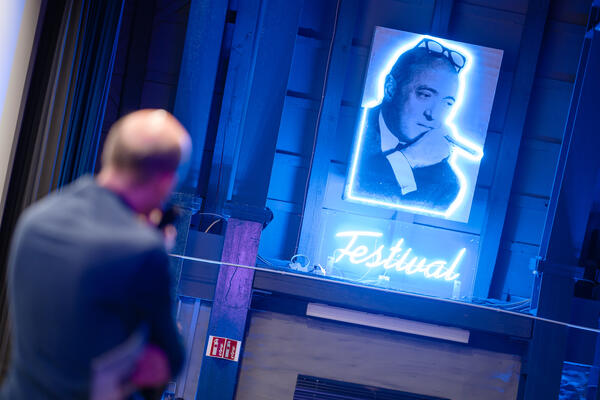 Person von hintern die auf Leuchtbild blickt auf dem Max Ophüls mit Zigarre abgebildet ist. unter dem Bild steht in Leuchtschrift Festival