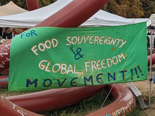 Ein grüner Banner hängt an einem roten Gerüst. Darauf steht: For Food Sovereignty &amp; Global Freedom of Movement!