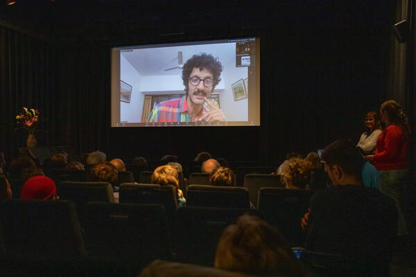 Blick von der Seite in der Mitte des Kinosaals im Koki. Links ein Blumenstrauß, in der Mitte die Leinwand mit Arjun Talwar, rechts zwei Frauen der Polnischen Frauen Solidarisch und vorne Kinopublikum von hinten zu sehen.