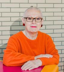 Ein Foto von Nora Eckert  knalloranger Pulli, rote Lippen, kurze graue Haare, eckige Brille