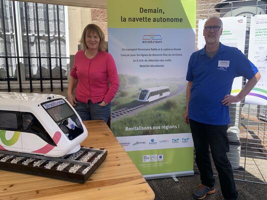Carola Wichert und Hannes Link am Infostand mit dem Mockup des autonom fahrenden Vehikels "Ecotrain" am Bahnhof Volgelsheim
