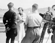 Leni Riefenstahl unterhält sich vor laufender Kamera mit Heinrich Himmler links im Bild. Rechts stehen ein dreiköpfiges männliches Kamerateam und im Hintergrund ein SA-Mitglied.