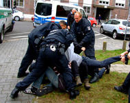 Mehrere deutsche Polizisten, die gewaltsam gegen Protestierende vorgehen, die auf dem Boden liegen.
