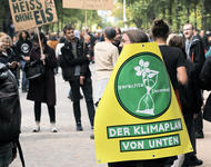 Ein Mensch läuft auf einer Demonstration mit einem Schild: Gerechte1komma5 - Der Klimaplan von unten
