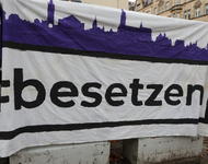 Ein Banner, auf dem "#besetzen" steht und eine Stadtsilhouette in violett gemalen ist.