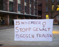 Ein weißes Transparent auf dem Platz der Alten Synagoge, auf dem steht: "25. November - Stopp Gewalt an Frauen". Ergänzt durch das Frauensymbol in der rechtsobigen Ecke und Handabrücke auf der Unterseite.