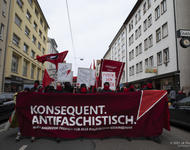 Demonstrationsfront mit rotem Transparent auf dem in weißen Großbuchstaben steht: Konsequent antifaschistisch.