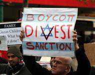 Ein Demonstrant hält ein Plakat in die Höhe, auf dem über die Fahne Israels in roten Lettern steht: Boycott - Divest - Sanction