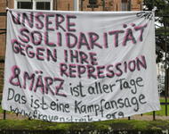 Ein Transparent hängt an einem Geländer, darunter steht ein rot-weißes Megafon. Auf dem Transparent steht: Unsere Solidarität gegen ihre Repression - 8. März ist aller Tage. Das ist eine Kampfansage (www.frauenstreik.org)